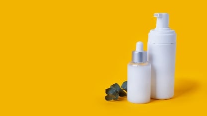 Weiße Kunststoff-Kosmetikpumpflaschen und Tropfflaschen auf gelbem Hintergrund mit einem kleinen Eukalyptuszweig.